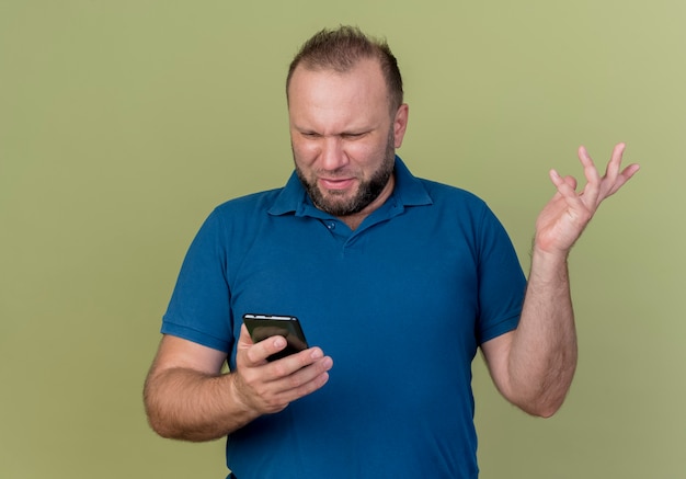 Hombre eslavo adulto disgustado sosteniendo y mirando el teléfono móvil mostrando la mano vacía