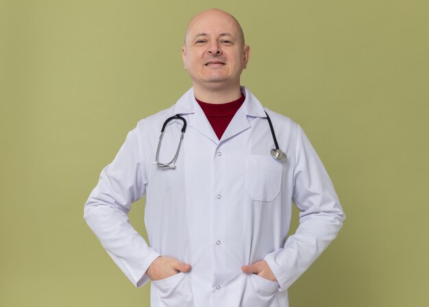 Hombre eslavo adulto sonriente en uniforme médico con estetoscopio mirando al frente