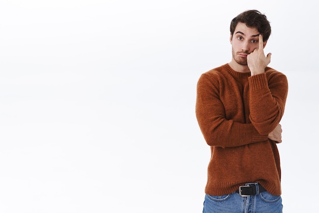 Hombre espaciando Joven molesto y tenso escuchando una conversación molesta y sin sentido cargada de información inútil parado pensativo tocando la frente y suspirando irritado harto