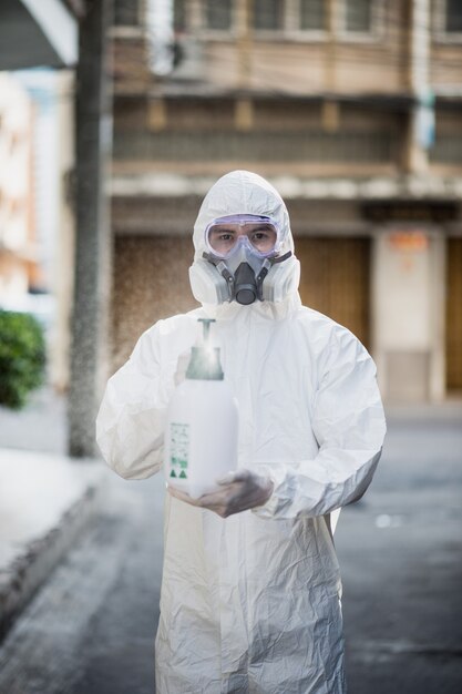 Hombre especialista en desinfección con traje de equipo de protección personal (EPI), guantes, mascarilla y protector facial, limpieza del área de cuarentena con una botella de desinfectante en aerosol presurizado para eliminar el coronavirus