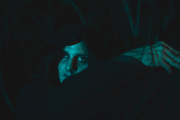 Hombre espeluznante con capucha sentado en la oscuridad