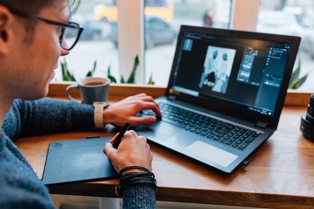 El hombre está editando fotos en la computadora portátil, usando una tableta gráfica y una pantalla con rotulador interactivo