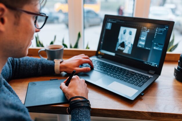 El hombre está editando fotos en la computadora portátil, usando una tableta gráfica y una pantalla con rotulador interactivo