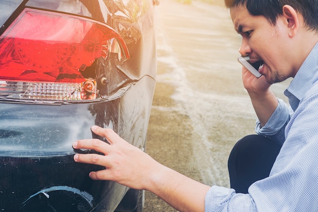 El hombre está llamando a la compañía de seguros por reclamar su accidente automovilístico dañado en accidente de tráfico