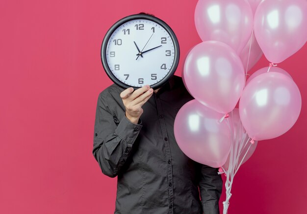 El hombre está parado con globos de helio sosteniendo y cerrando la cara aislada en la pared rosa