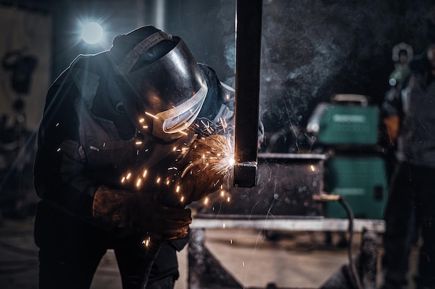 El hombre está trabajando en una fábrica de metal, está soldando un trozo de riel con herramientas especiales.