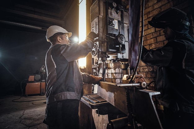 El hombre está trabajando con un taladro gigante en una concurrida fábrica de metal.