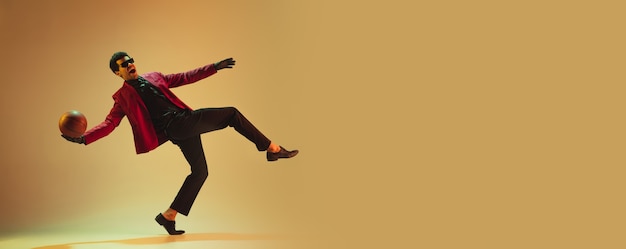 Hombre de estilo de alta costura en chaqueta roja jugando baloncesto aislado sobre pared marrón. Destacado deportista profesional afroamericano, realización de atletas, entrenamiento. Juventud, libertad, publicidad, ventas.