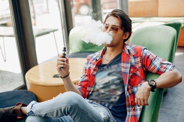 Hombre con estilo y elegante sentado en un café con vape