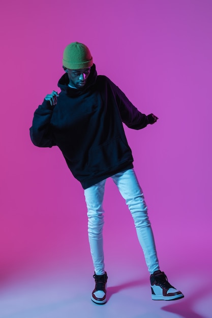 Hombre con estilo joven en traje moderno estilo callejero aislado en pared degradada en luz de neón Modelo de moda afroamericano en look book músico realizando