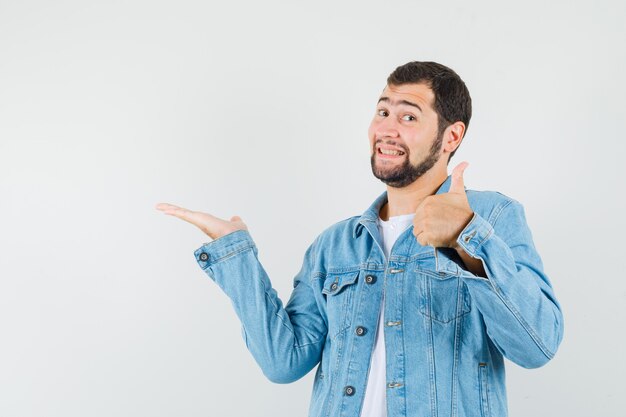 Hombre de estilo retro apuntando a un lado mientras muestra el pulgar hacia arriba en chaqueta, camiseta y luce positivo. vista frontal.