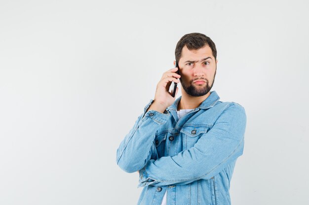 Hombre de estilo retro hablando por teléfono en chaqueta, camiseta y mirando pensativo, vista frontal.