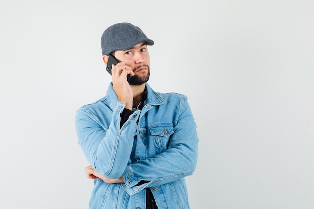 Hombre de estilo retro hablando por teléfono con chaqueta, gorra, camisa y mirando atento. vista frontal.