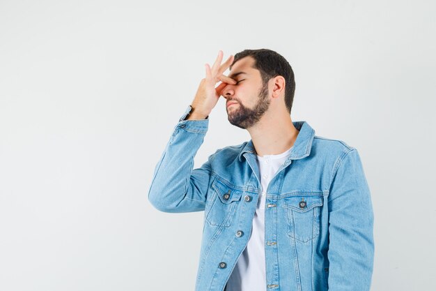 Hombre de estilo retro con la mano en la nariz en chaqueta, camiseta y luciendo incómodo.