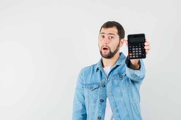 Hombre de estilo retro mostrando calculadora en chaqueta, camiseta y mirando sorprendido, vista frontal. espacio para texto