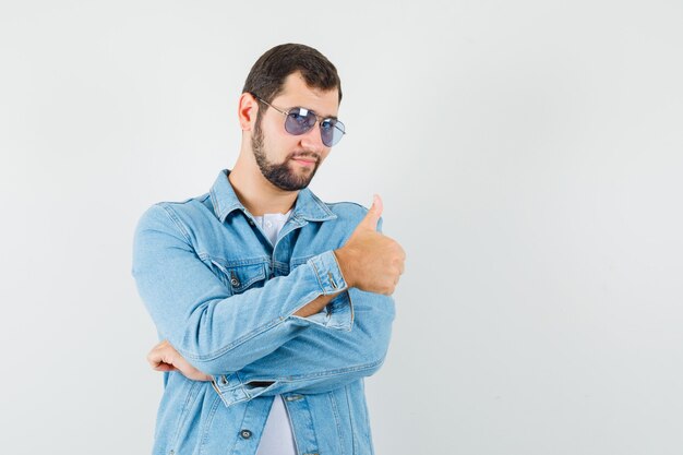 Hombre de estilo retro mostrando el pulgar hacia arriba en chaqueta, gafas de sol y mirando confiado, vista frontal.