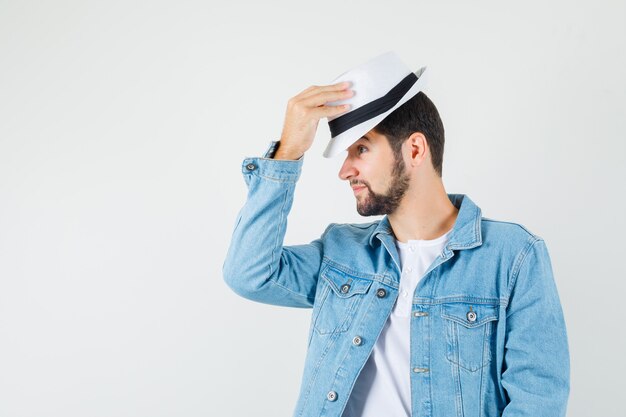 Hombre de estilo retro quitándose el sombrero con chaqueta, camiseta y luciendo satisfecho.