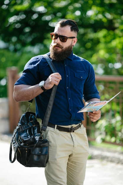 Hombre estiloso caminando con un mapa y un bolso