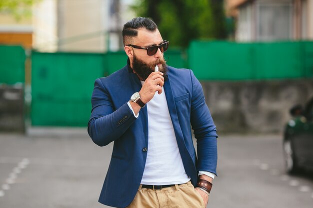 Hombre estiloso posando mientras fuma un cigarro electrónico