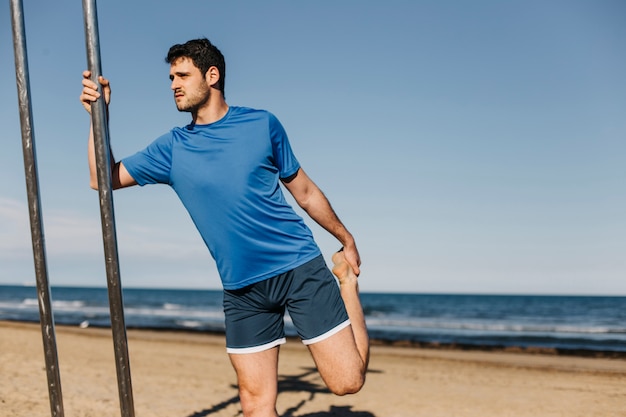 Hombre estirando en la playa con palo