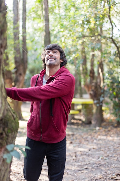 Hombre estirando su pierna junto a un árbol