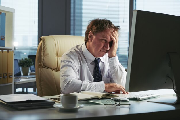 Hombre estresado con dolor de cabeza trabajando temprano en la mañana en su oficina