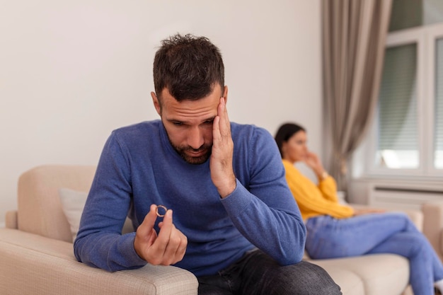 Un hombre estresado sosteniendo su anillo de bodas preocupado por la ruptura o el divorcio evita hablar con su esposa después de pelear una pareja ansiosa se ignora mutuamente El esposo triste y frustrado se quita el anillo de bodas