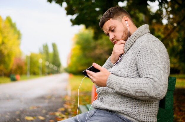 Hombre estresado con teléfono inteligente y auriculares en un banco