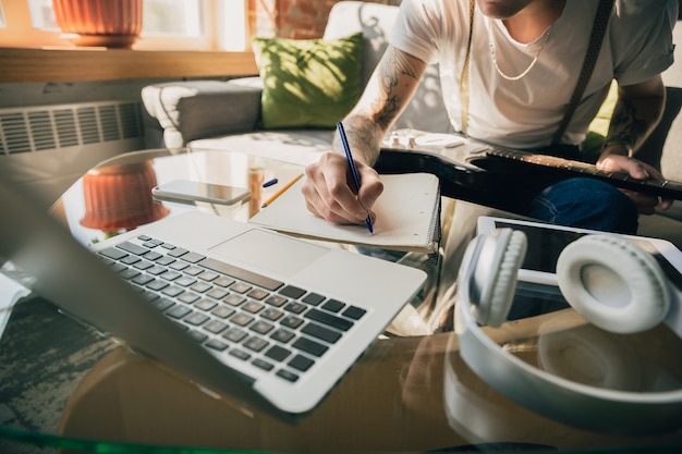 Foto gratuita hombre estudiando en casa durante cursos en línea o información gratuita por sí mismo. se convierte en músico, guitarrista en aislamiento, cuarentena contra la propagación del coronavirus. usando computadora portátil, teléfono inteligente, auriculares.