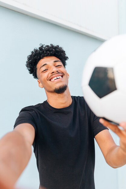 Hombre étnico sonriente con el fútbol que mira la cámara