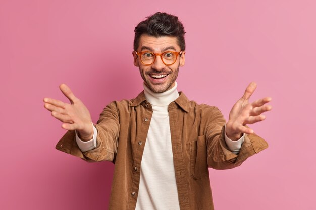 El hombre europeo amistoso positivo levanta las manos cuando se encuentra con alguien tira de los brazos en gesto de bienvenida