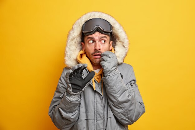 Hombre europeo asustado en ropa de abrigo con capucha de piel descansa en las montañas disfruta de deportes extremos tiene ocio activo durante la temporada de frío.