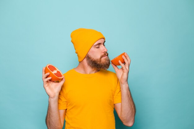 Hombre europeo barbudo en camisa amarilla aislado, oliendo delicioso pomelo con los ojos cerrados