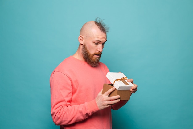 Hombre europeo barbudo en melocotón casual aislado, caja de regalo de apertura emocionada