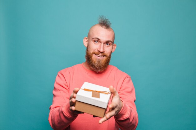 Hombre europeo barbudo en melocotón casual aislado, feliz sostiene caja de regalo