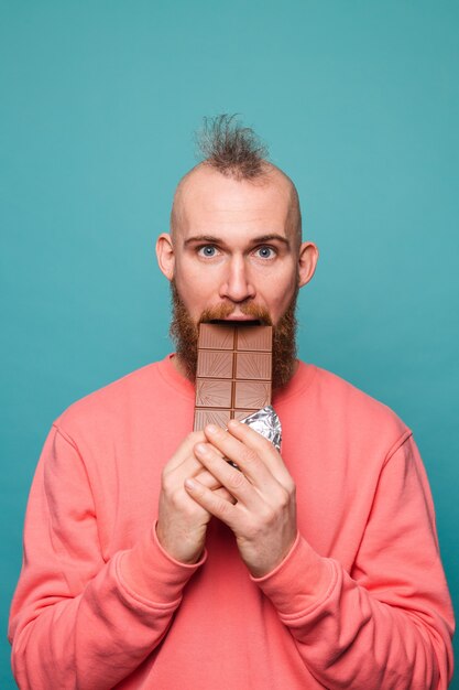 Hombre europeo barbudo en melocotón casual aislado, mordiendo chocolate