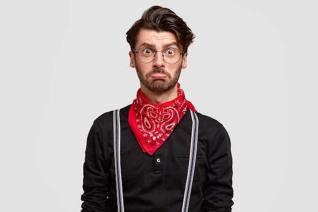 Hombre europeo insultado y disgustado con barba espesa, labio inferior curvo, corte de pelo moderno, camisa de moda con pañuelo rojo