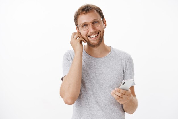 Hombre europeo seguro y agradable que firma acuerdos costosos en ir hablando con clientes en auriculares inalámbricos sosteniendo un teléfono inteligente y sonriendo amigable y alegre con una agradable conversación tranquila