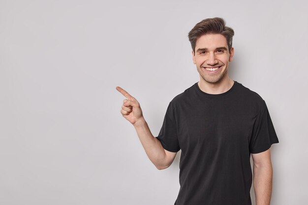 El hombre europeo sonriente con puntos de expresión alegres en el espacio en blanco muestra que la oferta de promoción demuestra que el anuncio usa una camiseta negra casual aislada sobre fondo blanco. Mira esto.