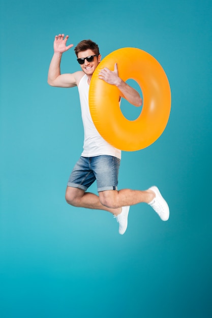 Hombre excitado feliz en gafas de sol con anillo inflable y saltando