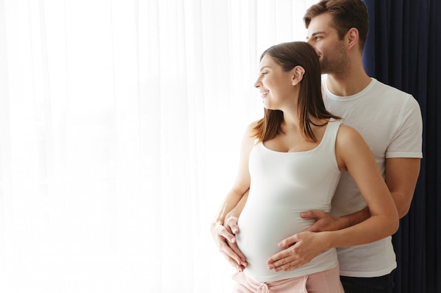 Hombre feliz abraza a su encantadora esposa embarazada en el interior en casa