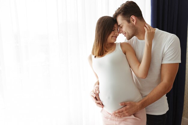Hombre feliz abraza a su encantadora esposa embarazada en el interior en casa
