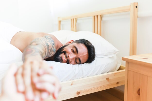 Hombre feliz acostado en la cama sosteniendo la mano de su novia