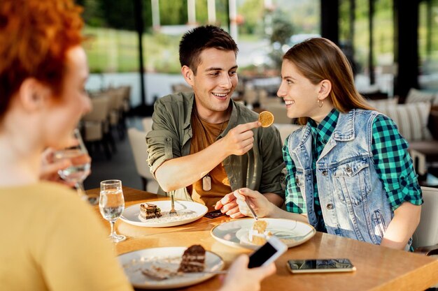 Hombre feliz alimentando a su novia mientras come postre en un café