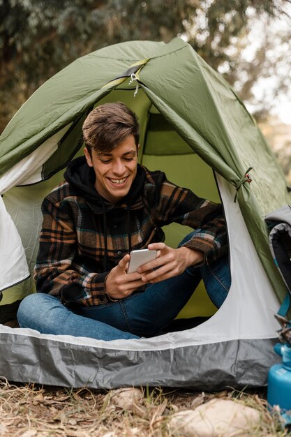 Hombre feliz camping en el bosque mediante teléfono móvil