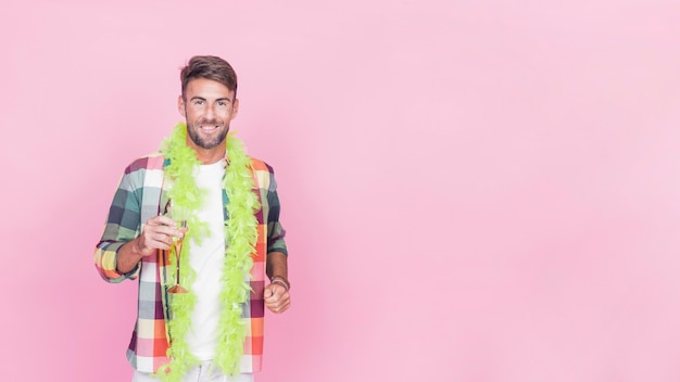 Hombre feliz celebración de flauta de champán con boa verde alrededor de su cuello de pie contra el fondo rosa