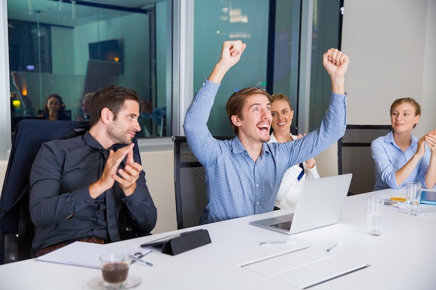 Hombre feliz celebrando con los puños en alto y sus compañeros le aplauden