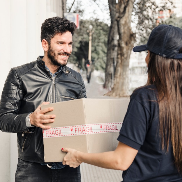 Hombre feliz en la chaqueta negra que recibe el paquete del mensajero femenino