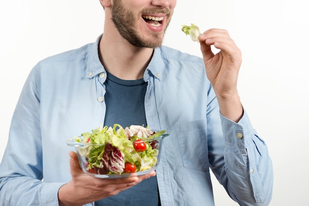 Hombre feliz comiendo ensalada saludable contra fondo blanco