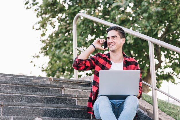 Hombre feliz con la computadora portátil hablando por teléfono móvil